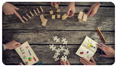 Illustration du management de la santé au travail : des mains devant des bouts de bois, des pièces de puzzle, des carnets avec des dessins et des crayons